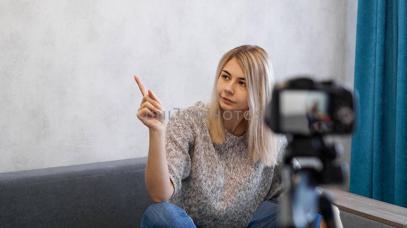 Young female blogger talks about business or records a lecture. Woman shows with on a gray wall. Place for information