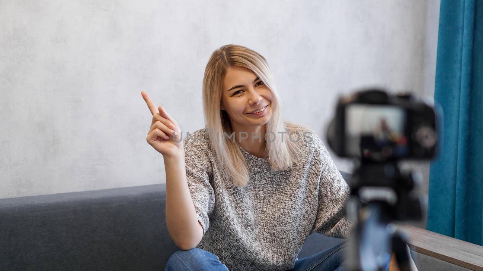 Young female blogger talks about business or records a lecture. Woman shows with on a gray wall. Place for information