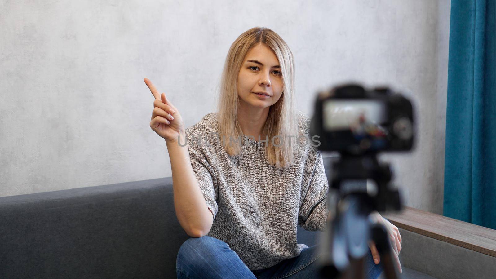 Young female blogger talks about business or records a lecture. Woman shows with on a gray wall. Place for information