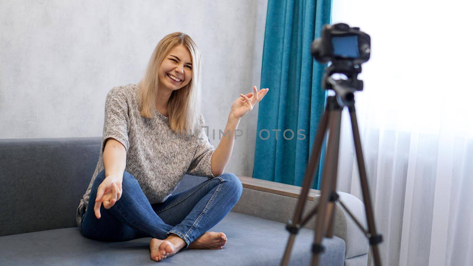 Happy female blogger telling joke and laughing while sitting on couch and recording video