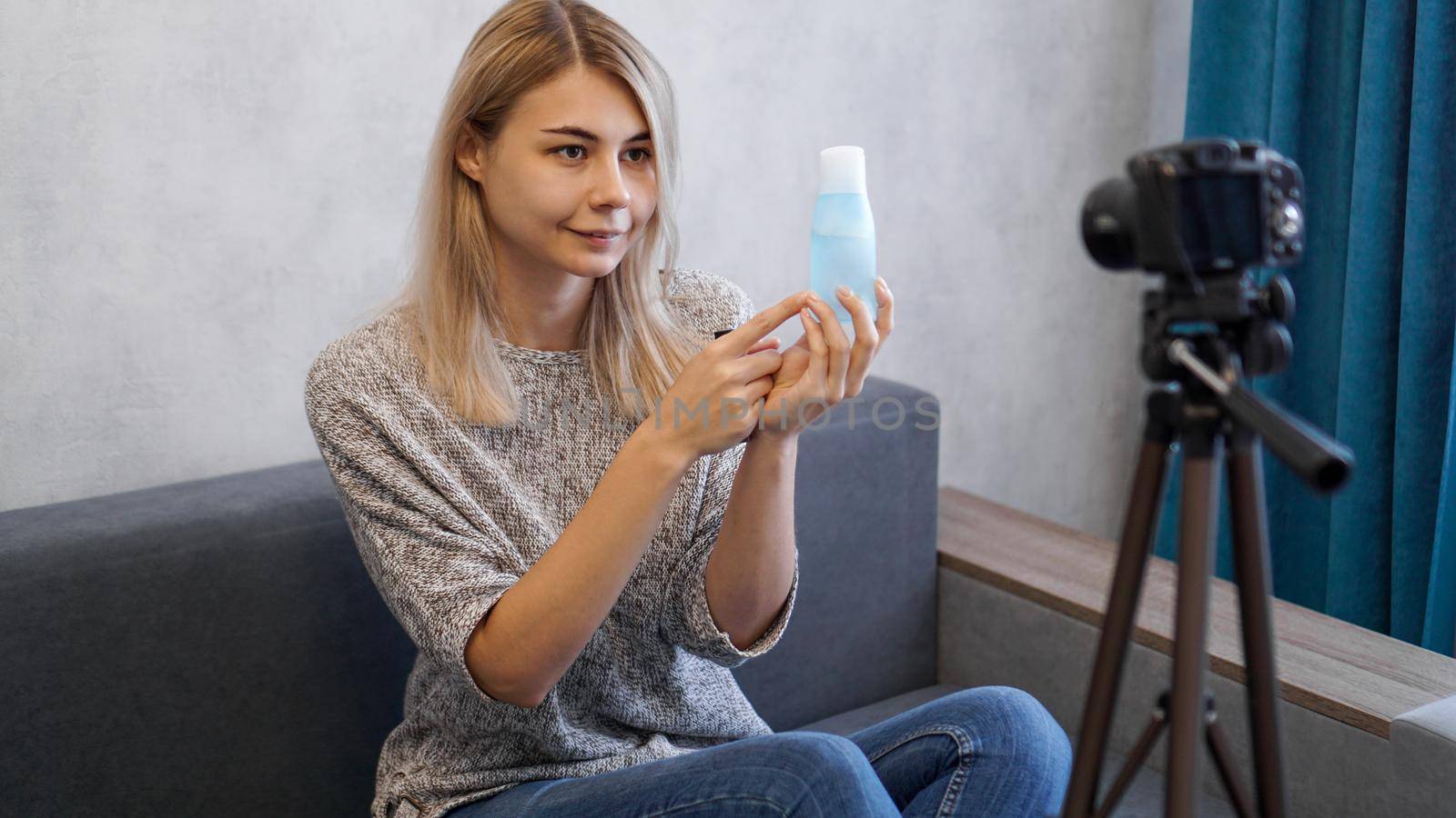Cheerful female beauty blogger recording video at home. She shows lotion for skin.