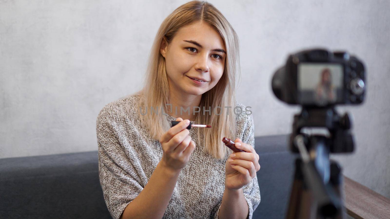 Vlogger female showing lipstick. Beauty blogger woman filming daily make-up routine tutorial near camera on tripod