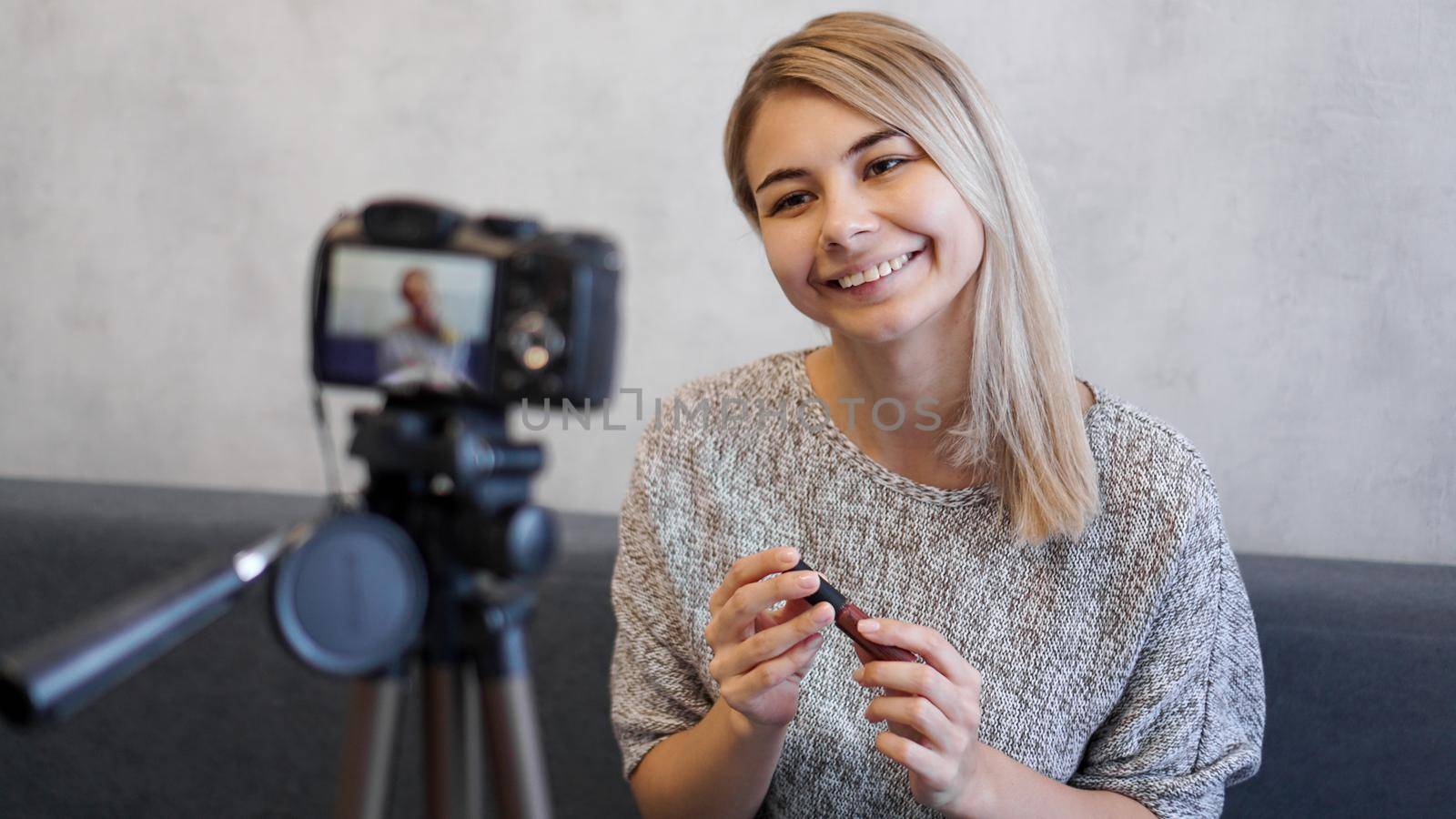 Vlogger female showing lipstick. Beauty blogger woman filming daily make-up routine tutorial near camera on tripod