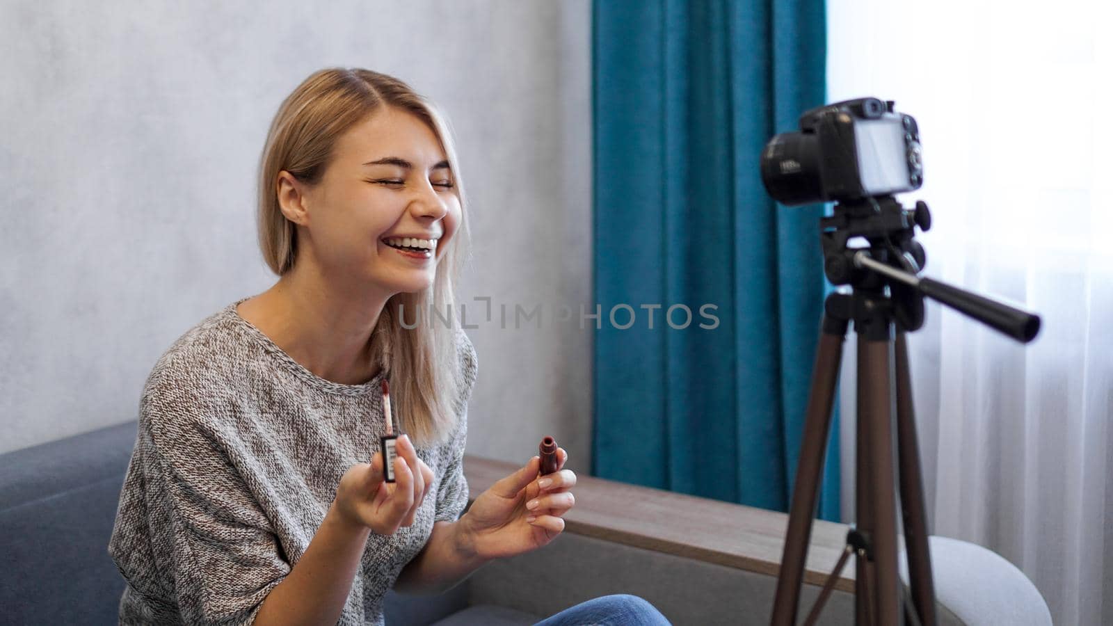 A beauty blogger or video blogger tells and shows subscribers how to do makeup. Young woman paints lips and laughs at a joke