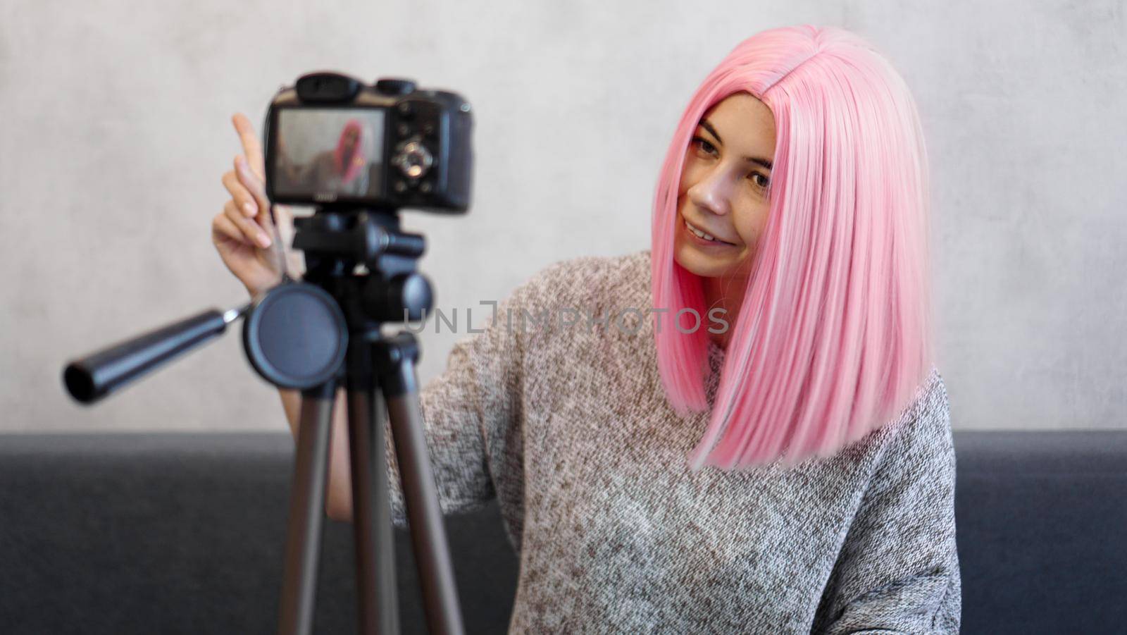 Happy girl blogger in pink wig in front of the camera on a tripod. She records a video blog and communicates with subscribers on social networks