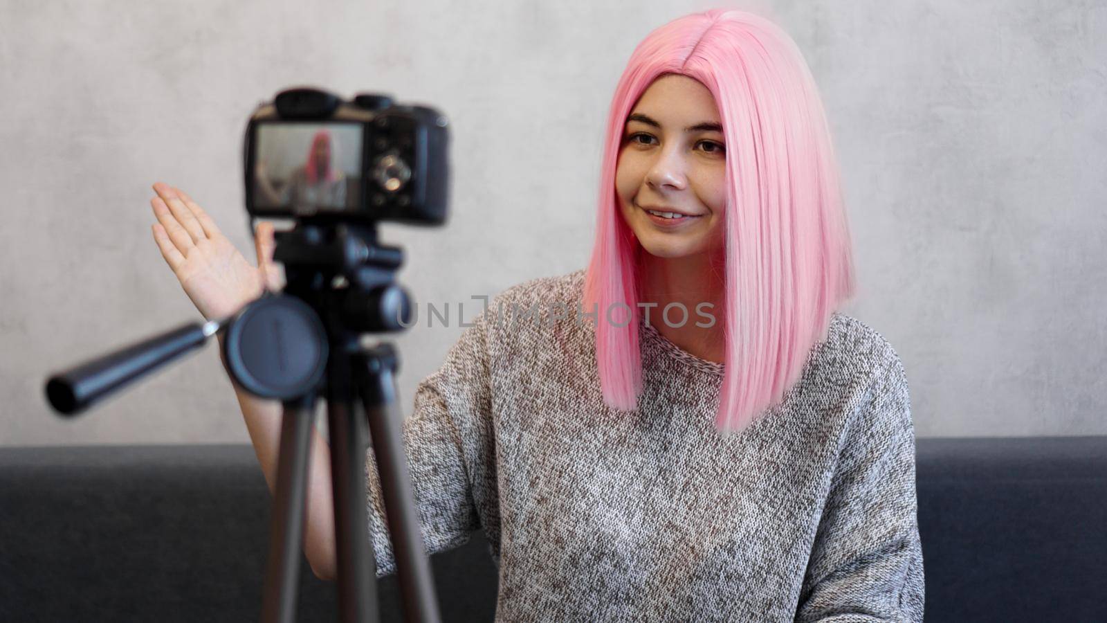 Happy girl blogger in pink wig in front of the camera on a tripod. She records a video blog and communicates with subscribers on social networks