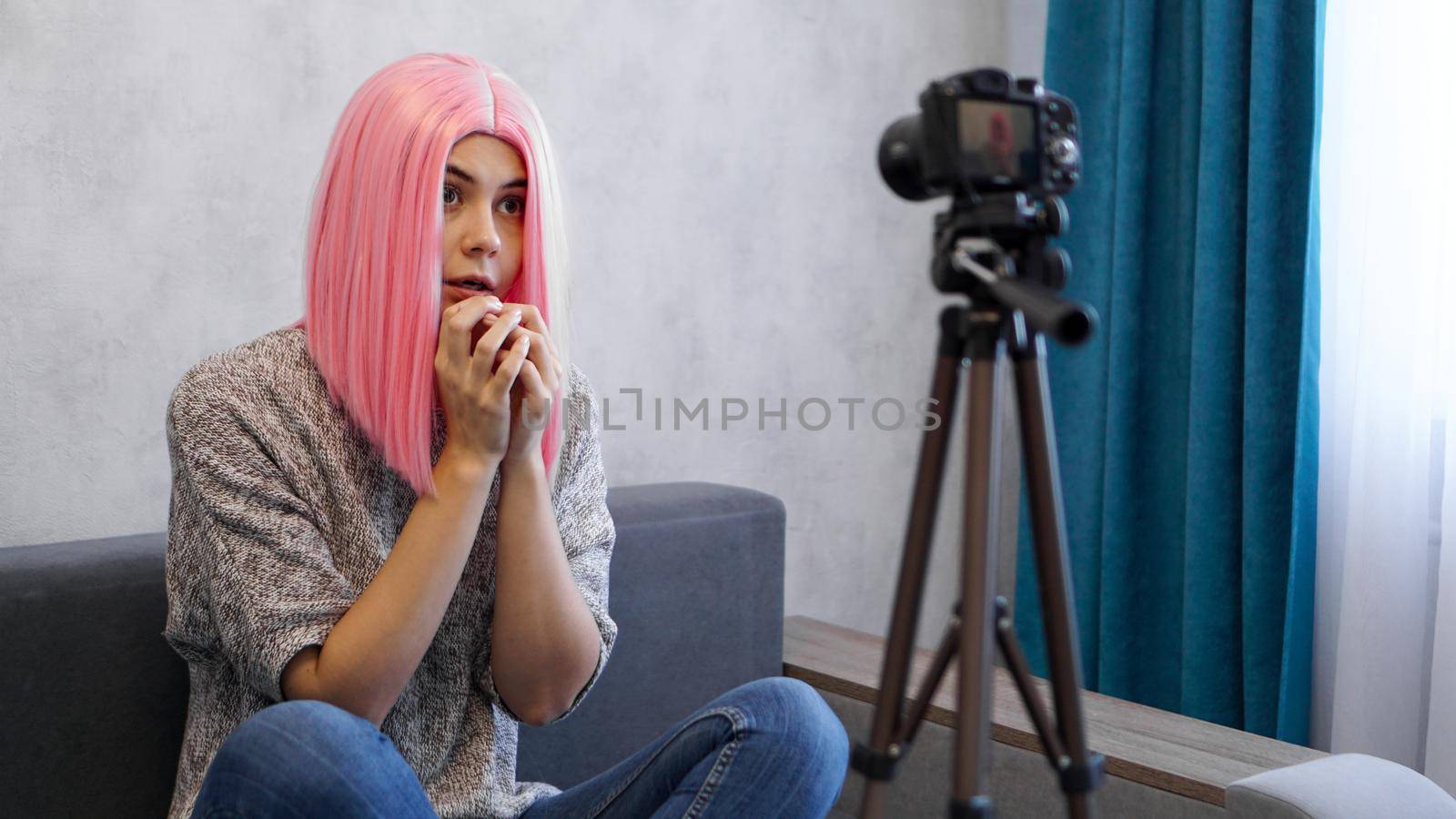 Young female blogger in pink wig with camera vlogging stressed
