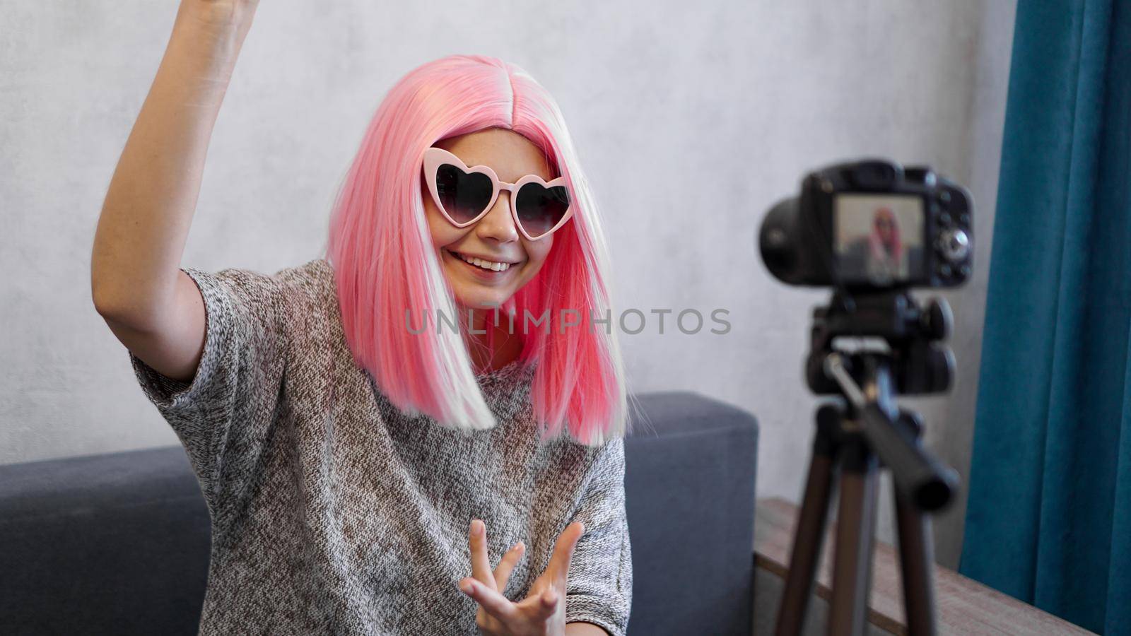 Happy girl blogger in pink wigs in front of the camera on a tripod. She records a video blog and communicates with subscribers on social networks.