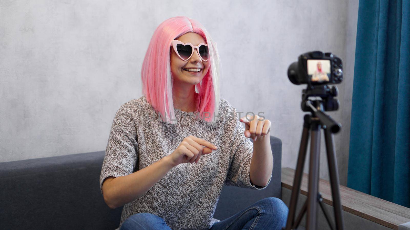 Happy girl blogger in pink wig in front of the camera on a tripod. She records a video blog