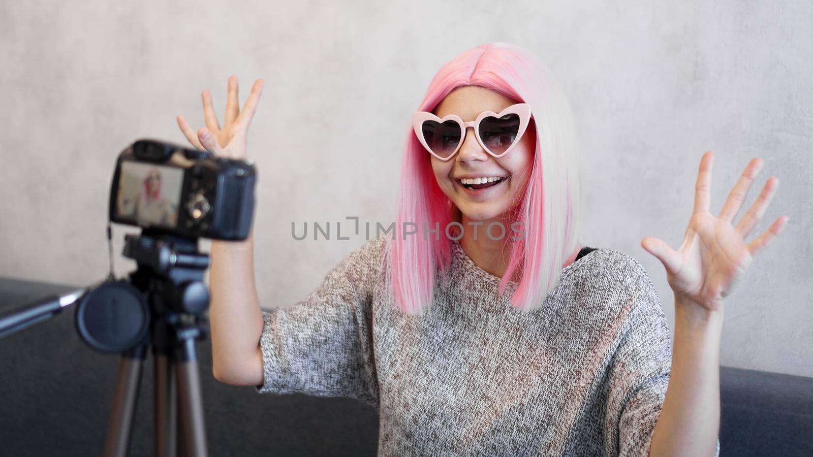 Happy girl blogger in pink wig in front of the camera on a tripod. She records a video blog