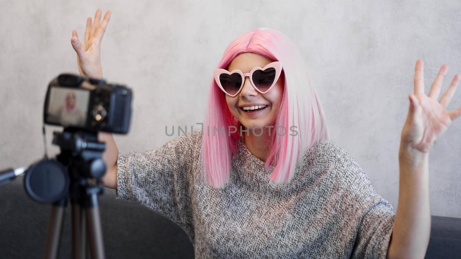 Happy girl blogger in pink wig in front of the camera on a tripod. She records a video blog