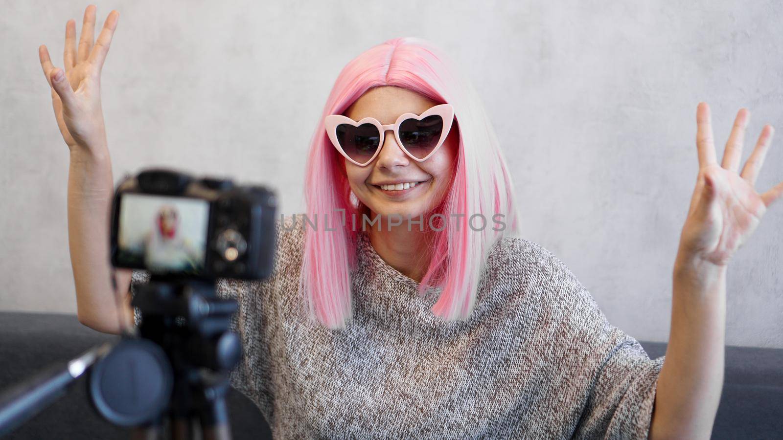 Happy girl blogger in pink wigs in front of the camera on a tripod. She records a video blog and communicates with subscribers on social networks.