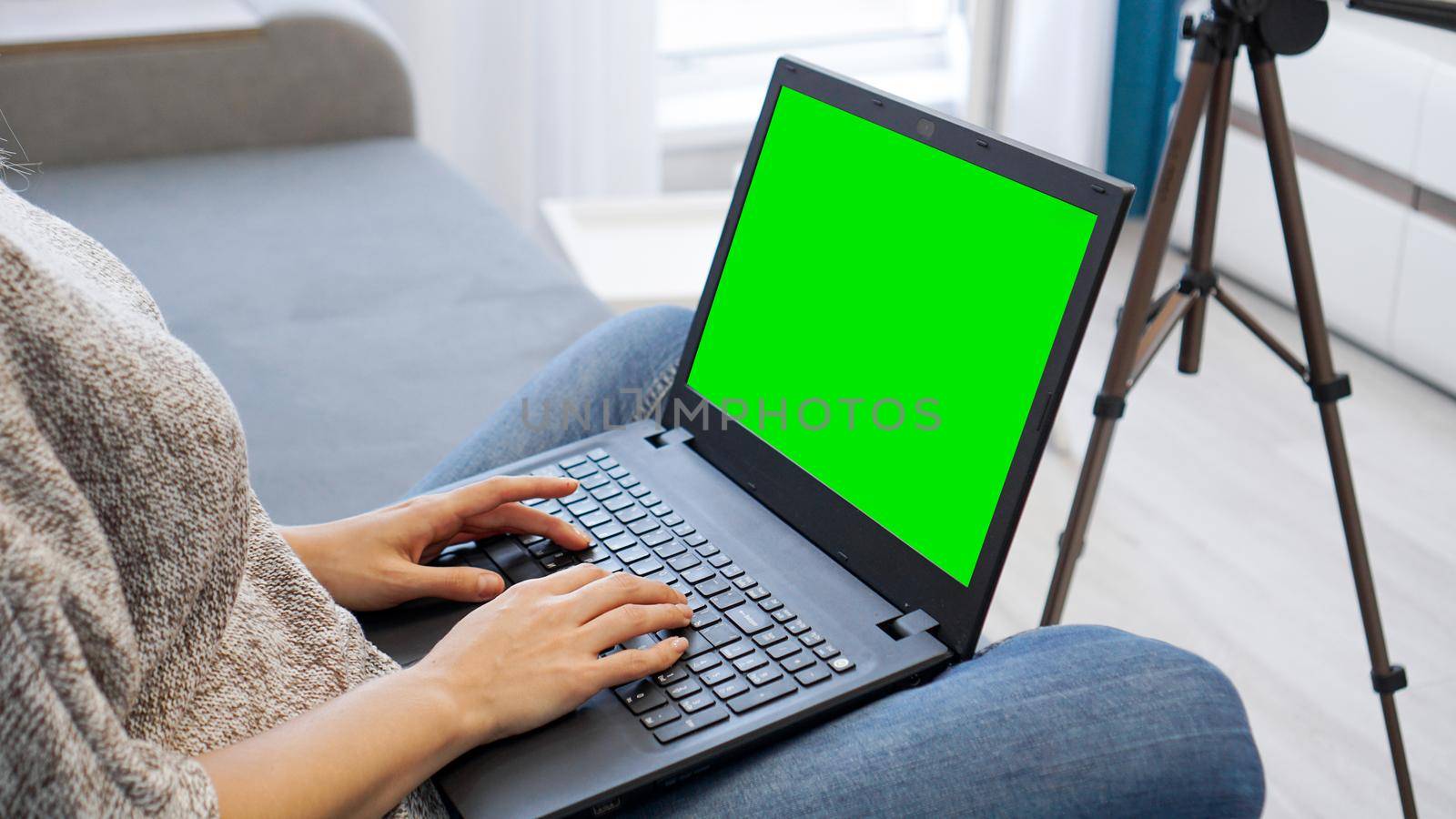 Woman blogger working on laptop. View of camera on tripod and laptop with green screen chromakey - close up view