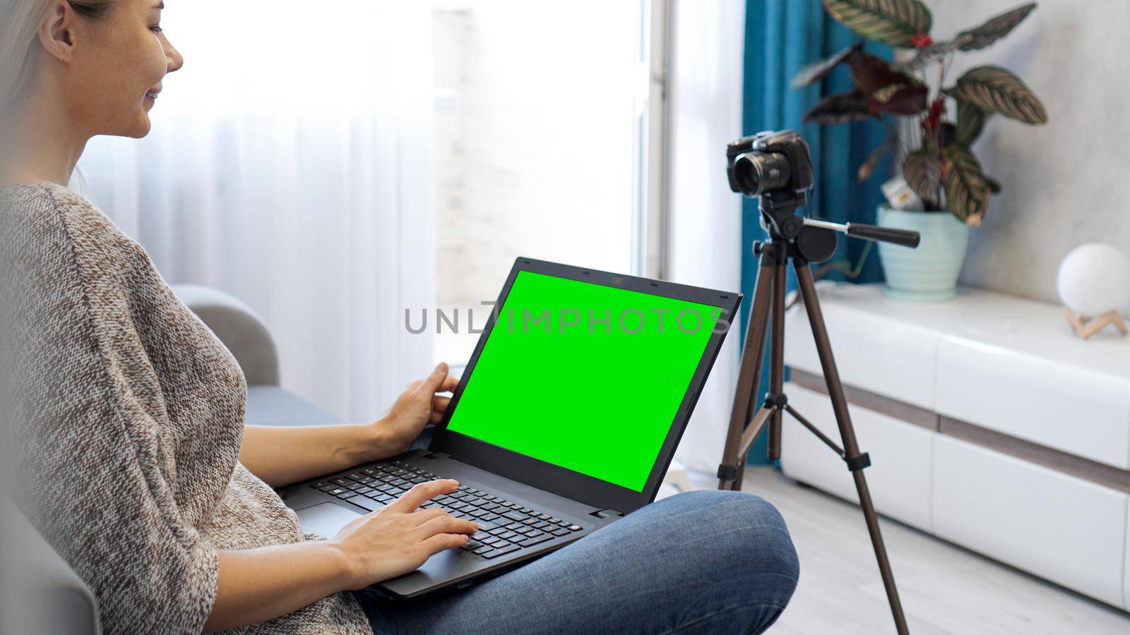 Woman blogger working on laptop. View of camera on tripod and laptop with green screen chromakey