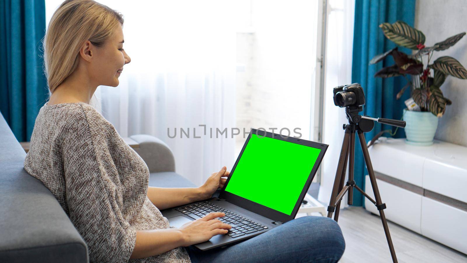 Woman blogger working on laptop. View of camera on tripod and laptop with green screen chromakey