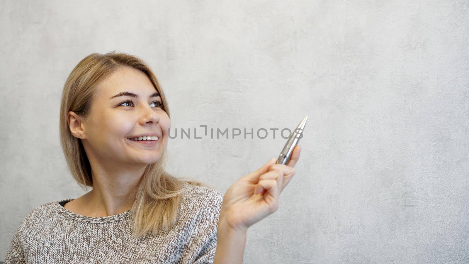 The woman shows with a pen on a gray wall. Place for information - graphics, inscriptions, banners