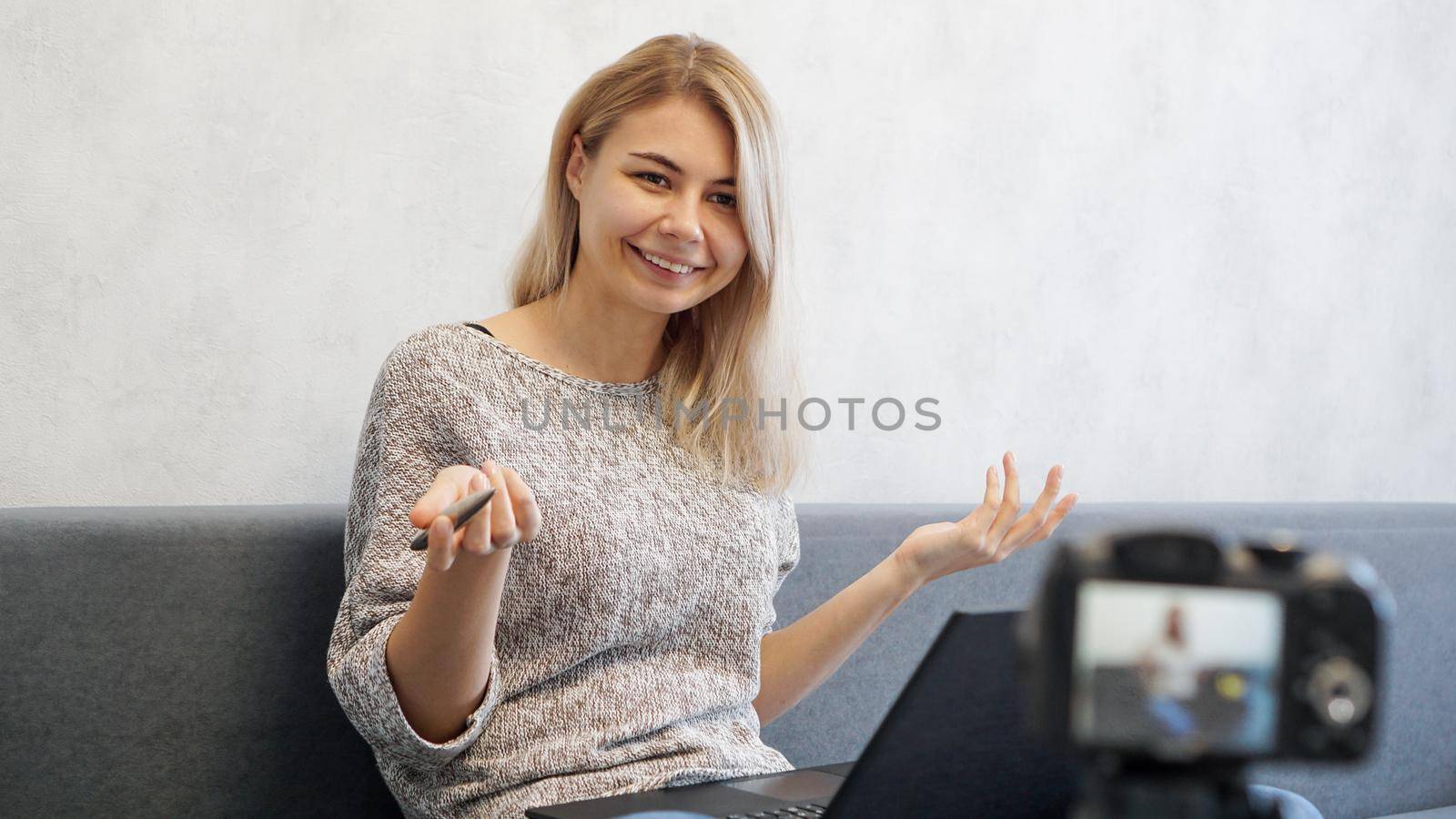 Young female blogger with laptop and pen looking at camera. She talks about business or records a lecture for students. She is positive and smiling.
