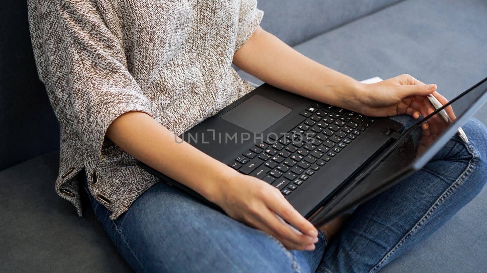 Woman using laptop with blank screen while sitting on sofa in home interior back view