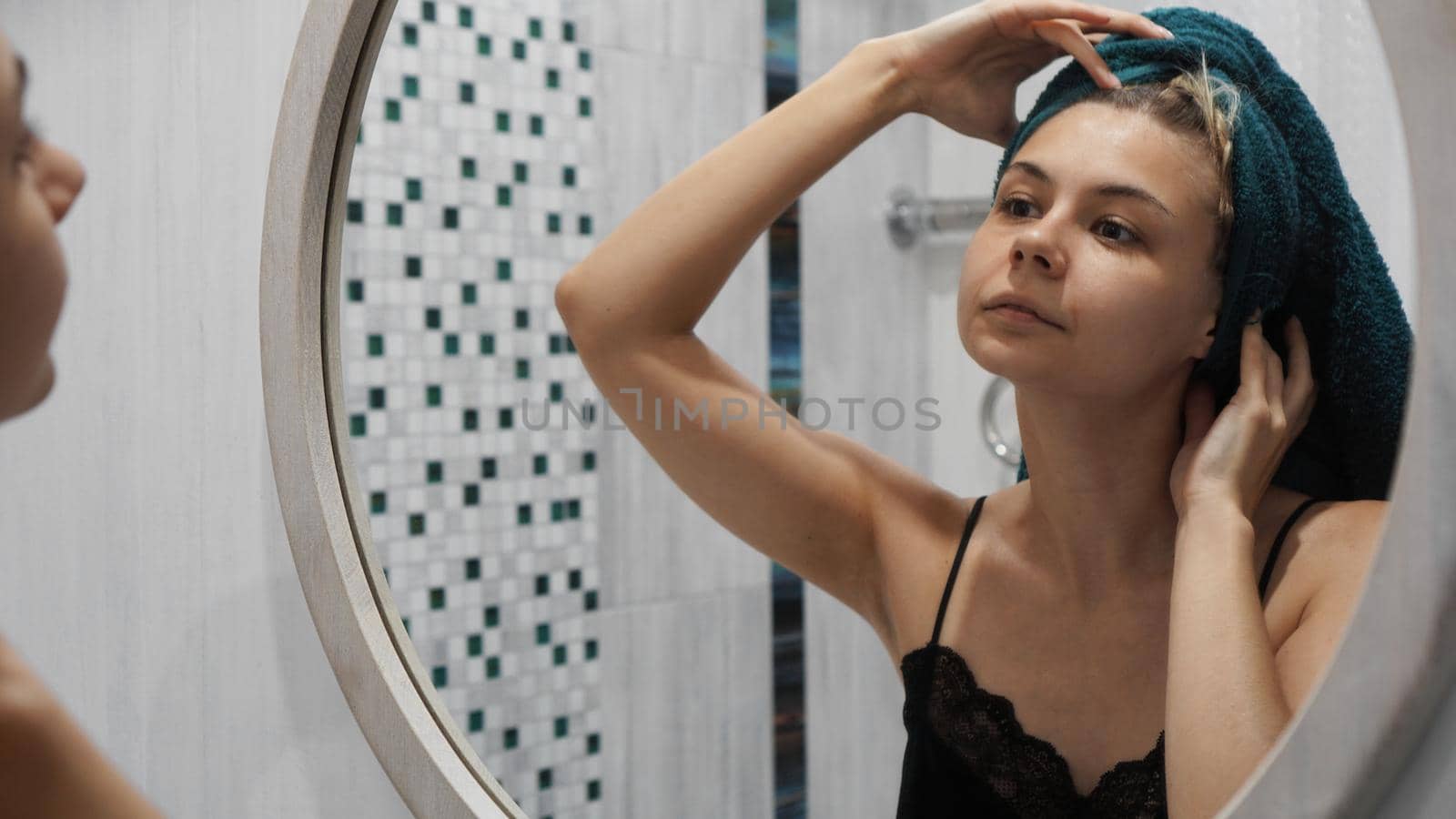 Woman with a towel on hair looks in the mirror in the bath room