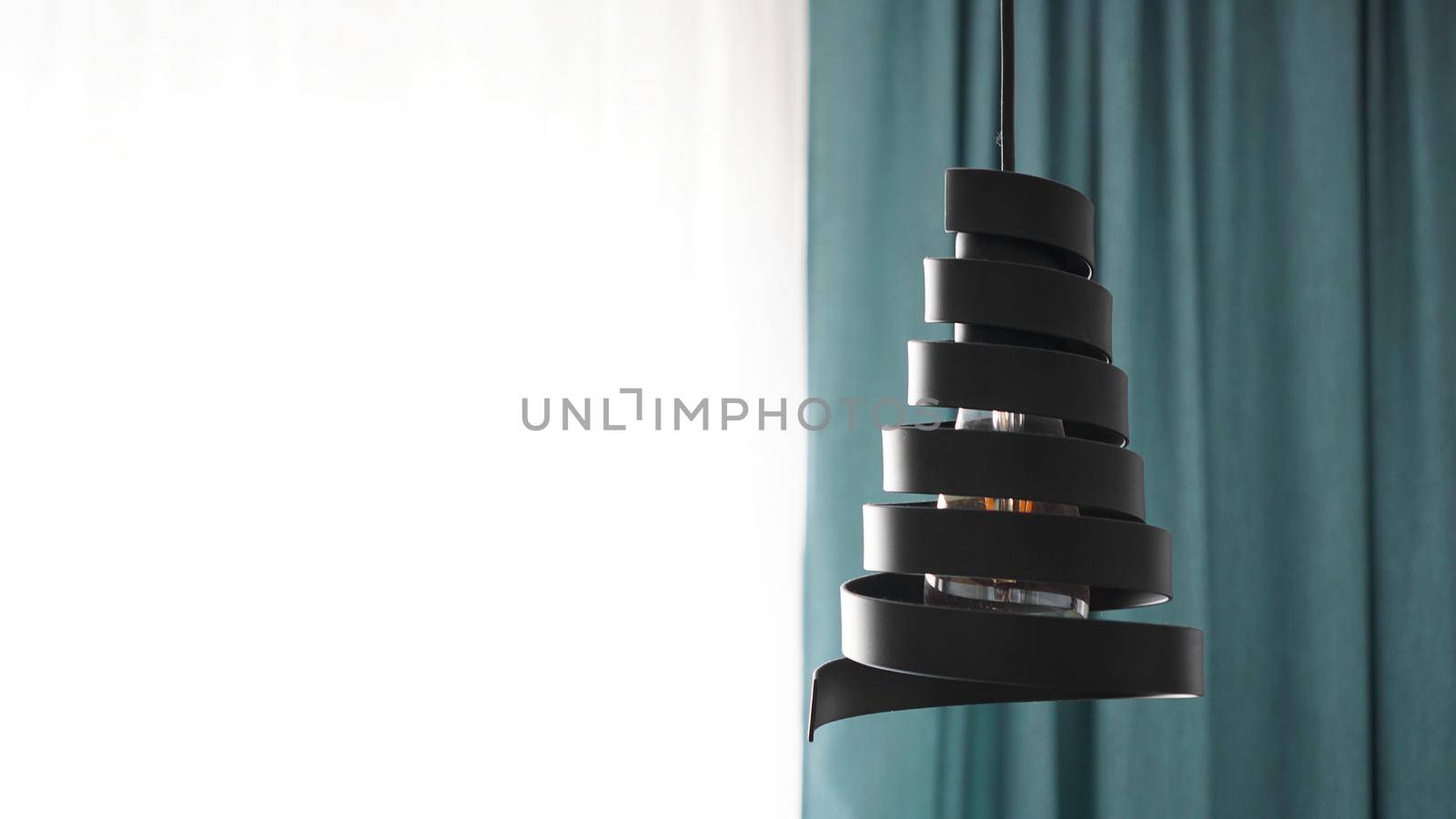 A modern loft chandelier made of black metal spiral in a stylish white and green interior