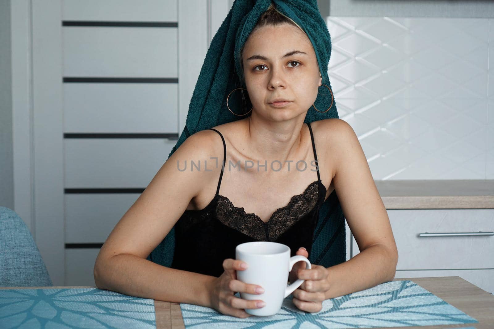Beautiful woman in a towel on hair with a cup of coffee. Woman looking at camera