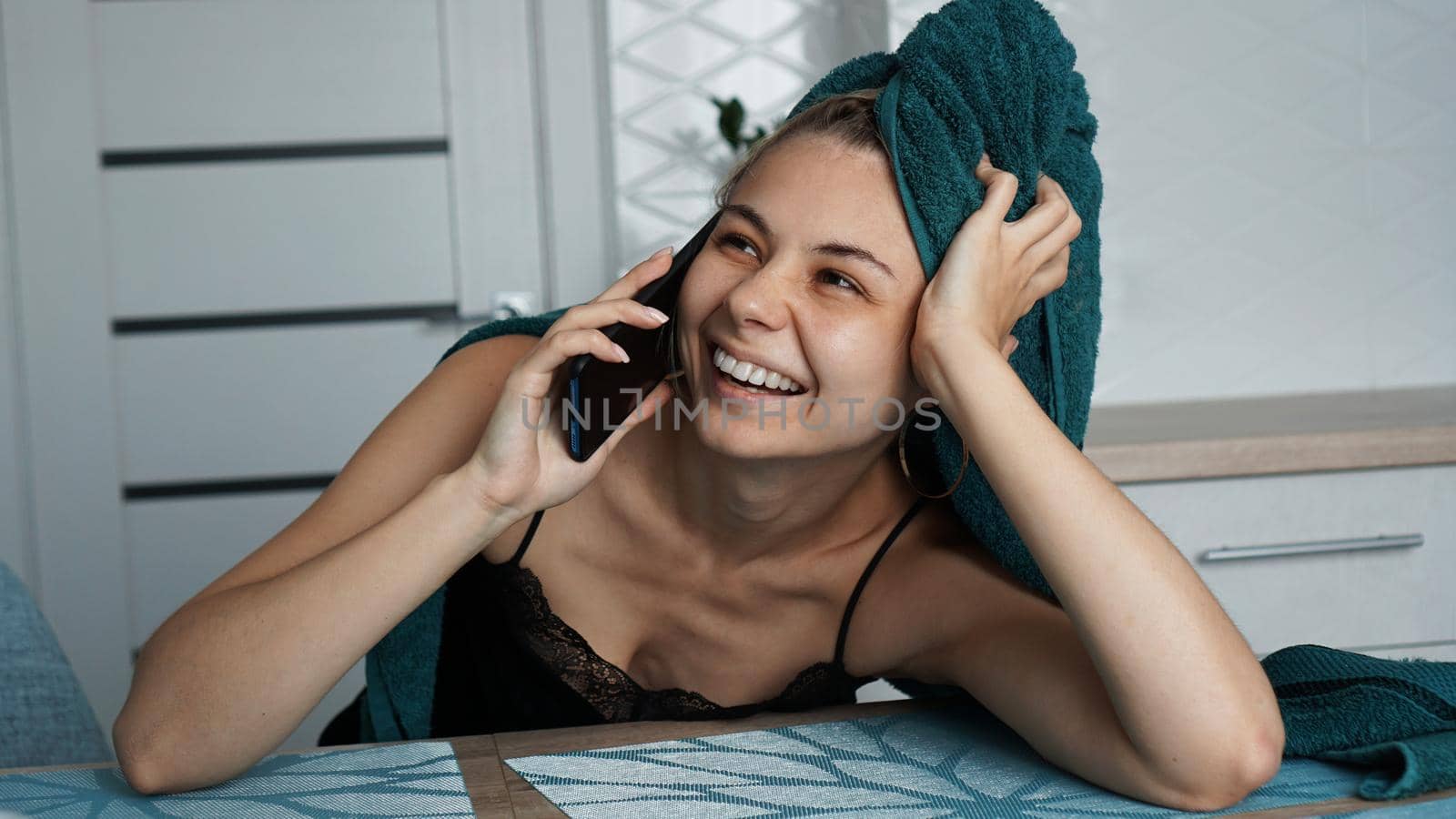 Young woman in kitchen. Talking on phone and smile. Breakfast after bathing. Woman in towel