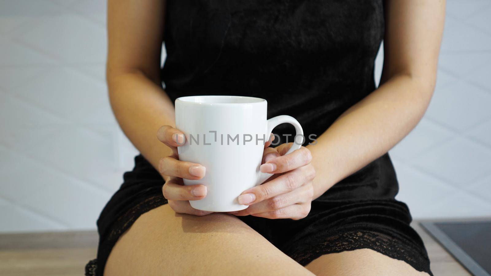 A closeup shot of the female holding a white cup in her hand at kitchen