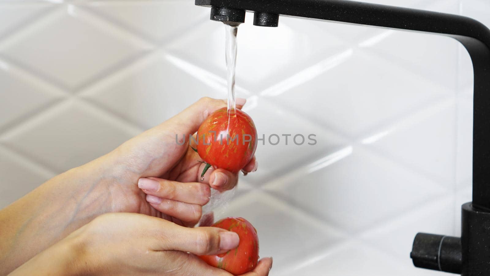 Woman washing tomatoes and tomato in her hands - white kitchen background