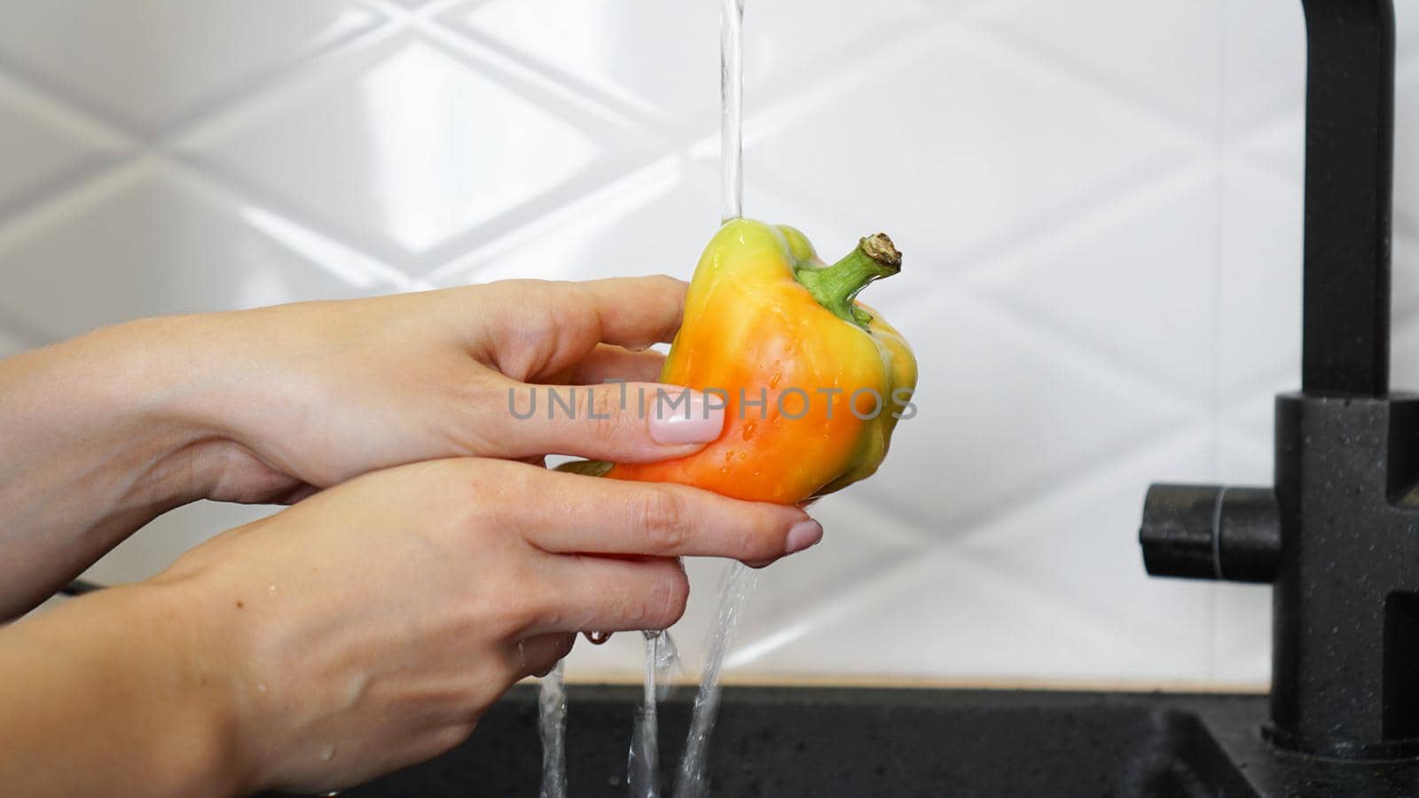 Female hands washing yellow and red color pepper. White kitchen background