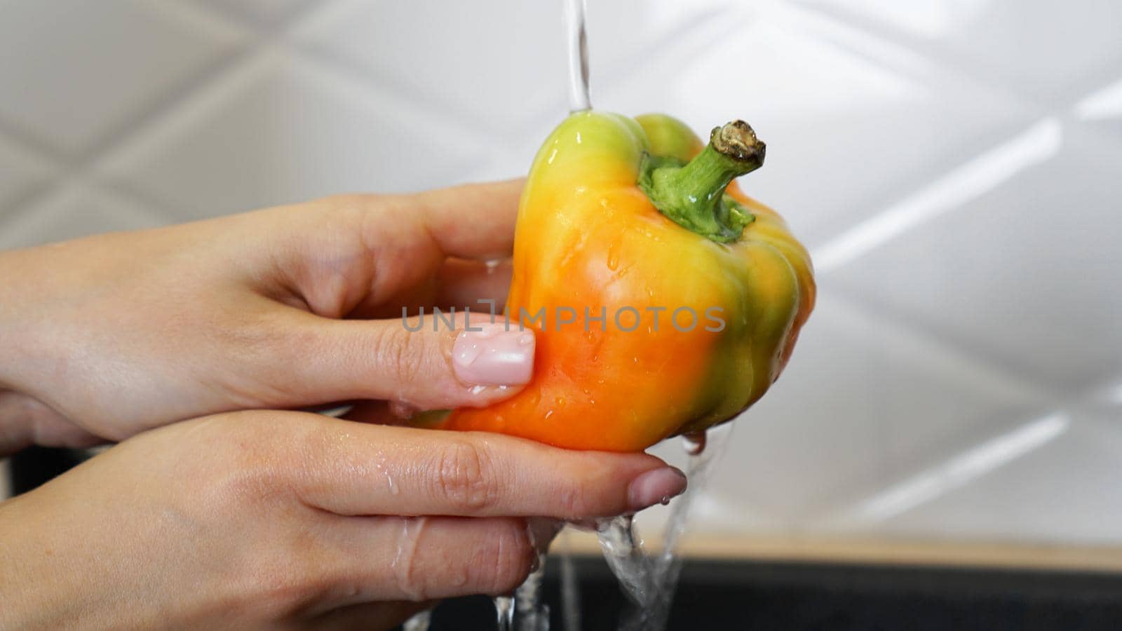 Female hands washing yellow and red color pepper. White kitchen background