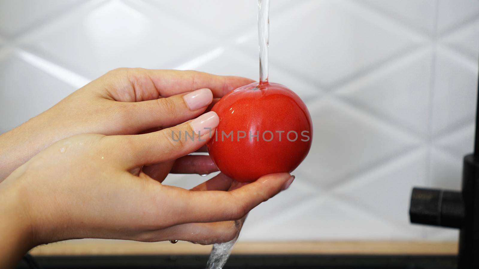 Woman washing tomatoes and tomato in her hands - white kitchen background