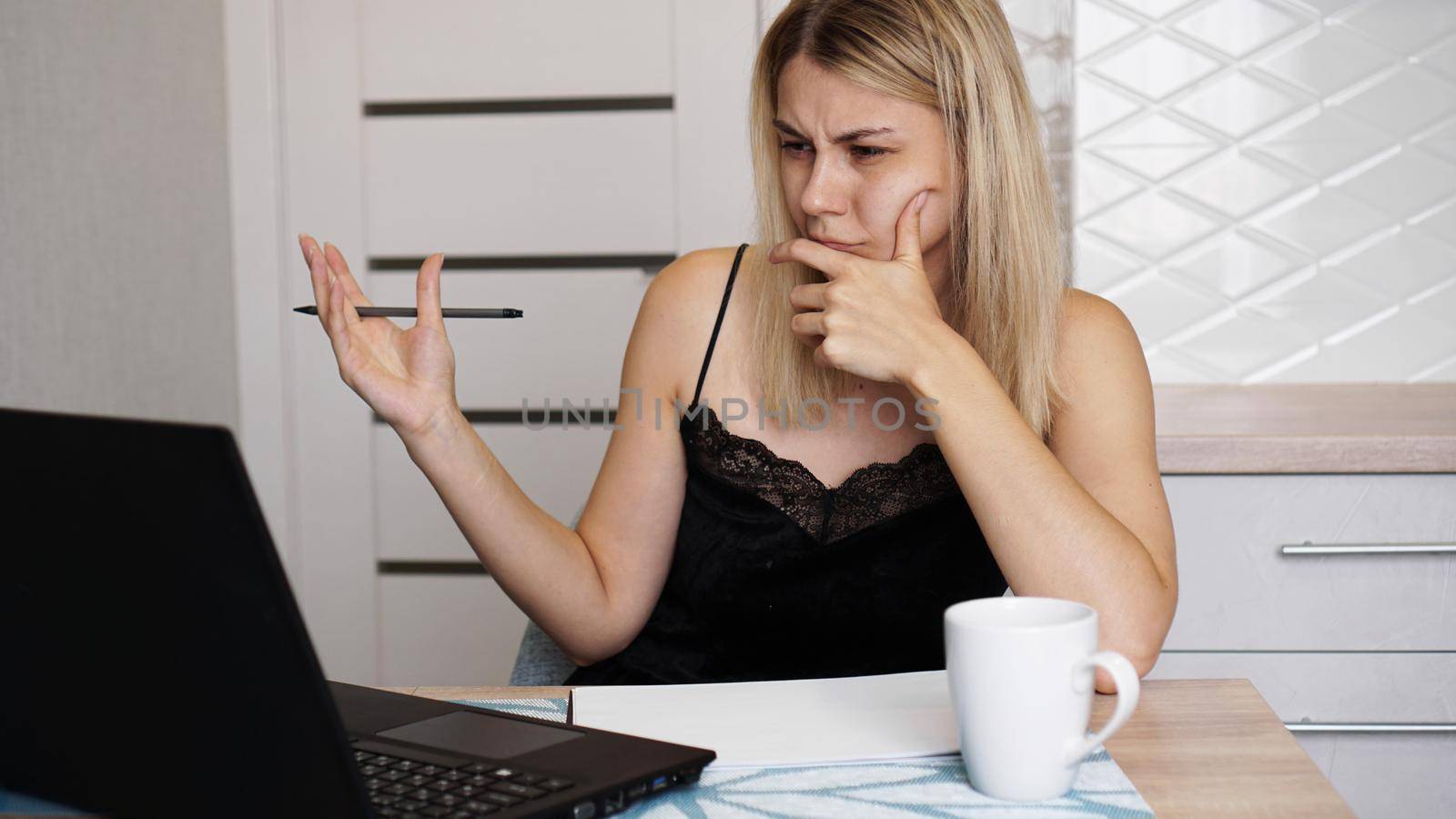 Portrait of an attractive woman at the table with cup and laptop. Confused young woman having problem with computer, looking at laptop screen