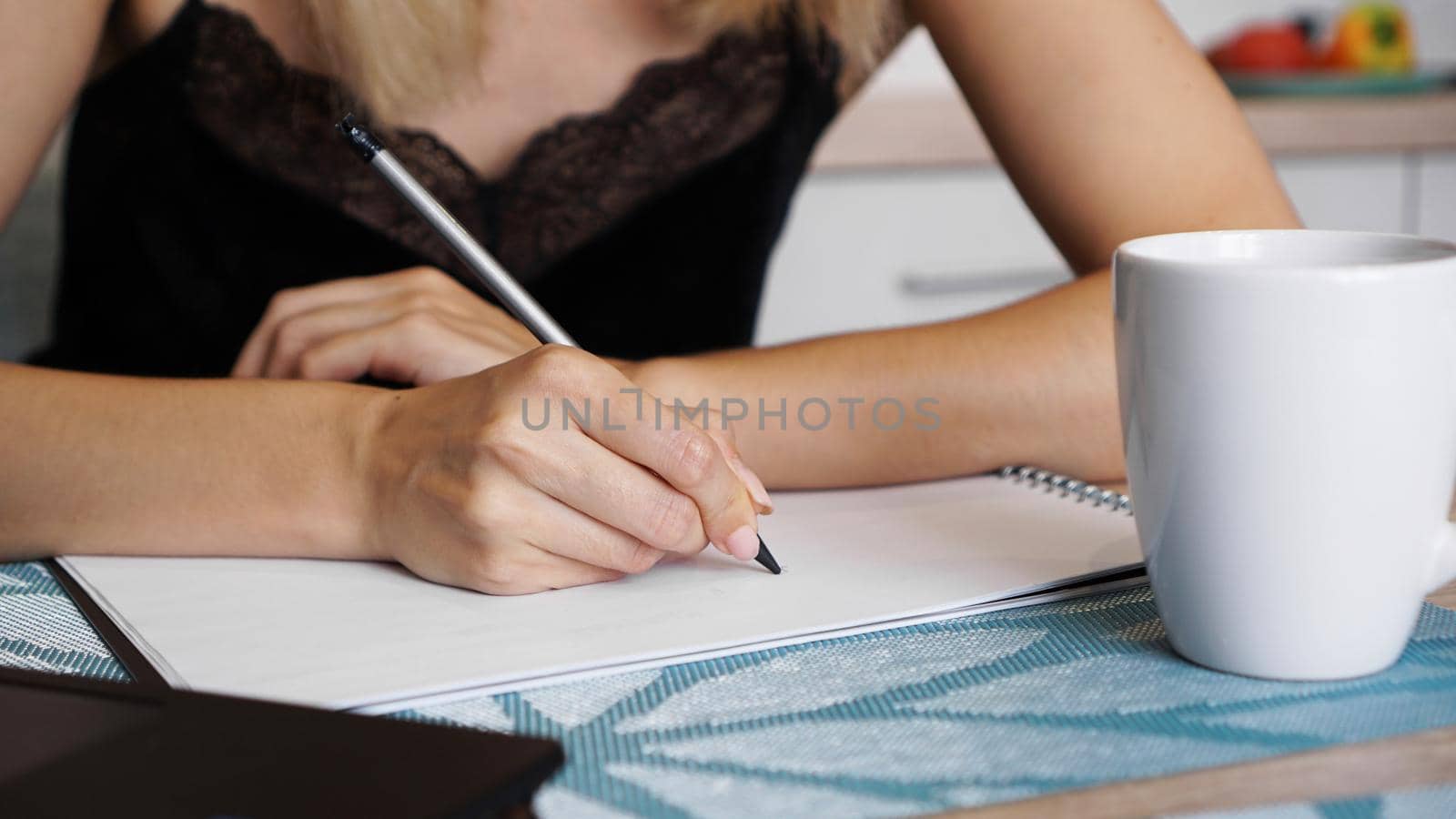 Woman hand use pencil writing on clear white sheet. White cup. Remote work or study