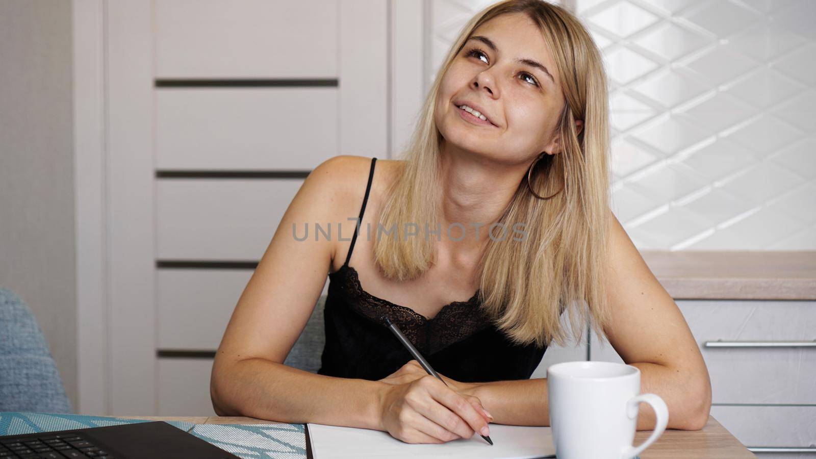 A woman sits in a bright kitchen and writes a letter or her wishes. A girl dreams. A cup of coffee is on the table.