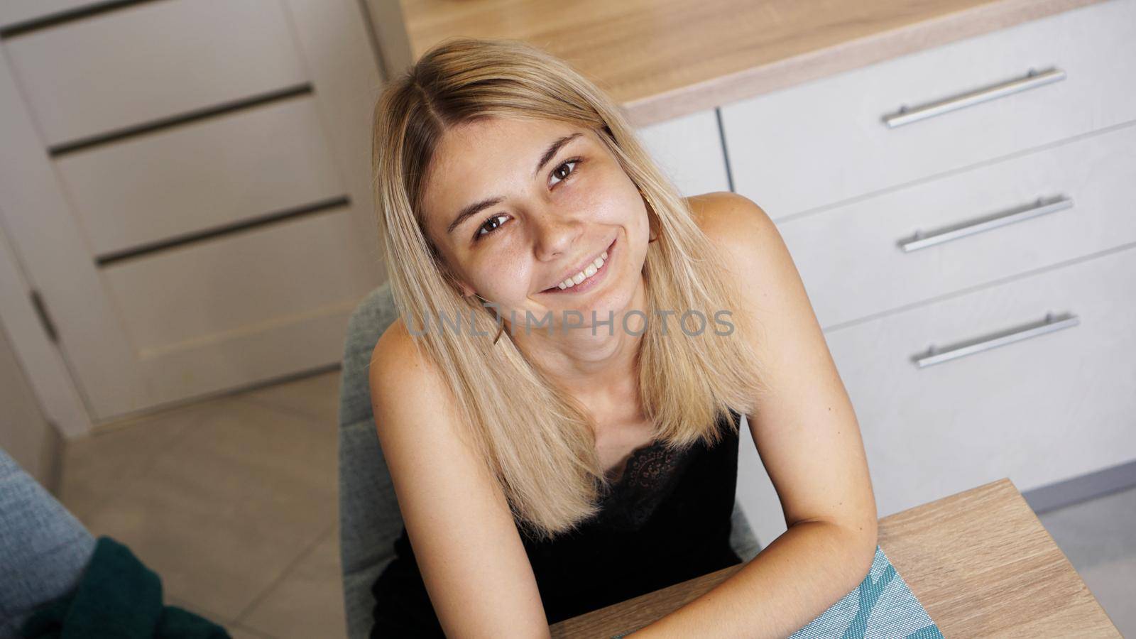 Cheerful young female sitting at table in cozy styled room while smiling and looking at camera