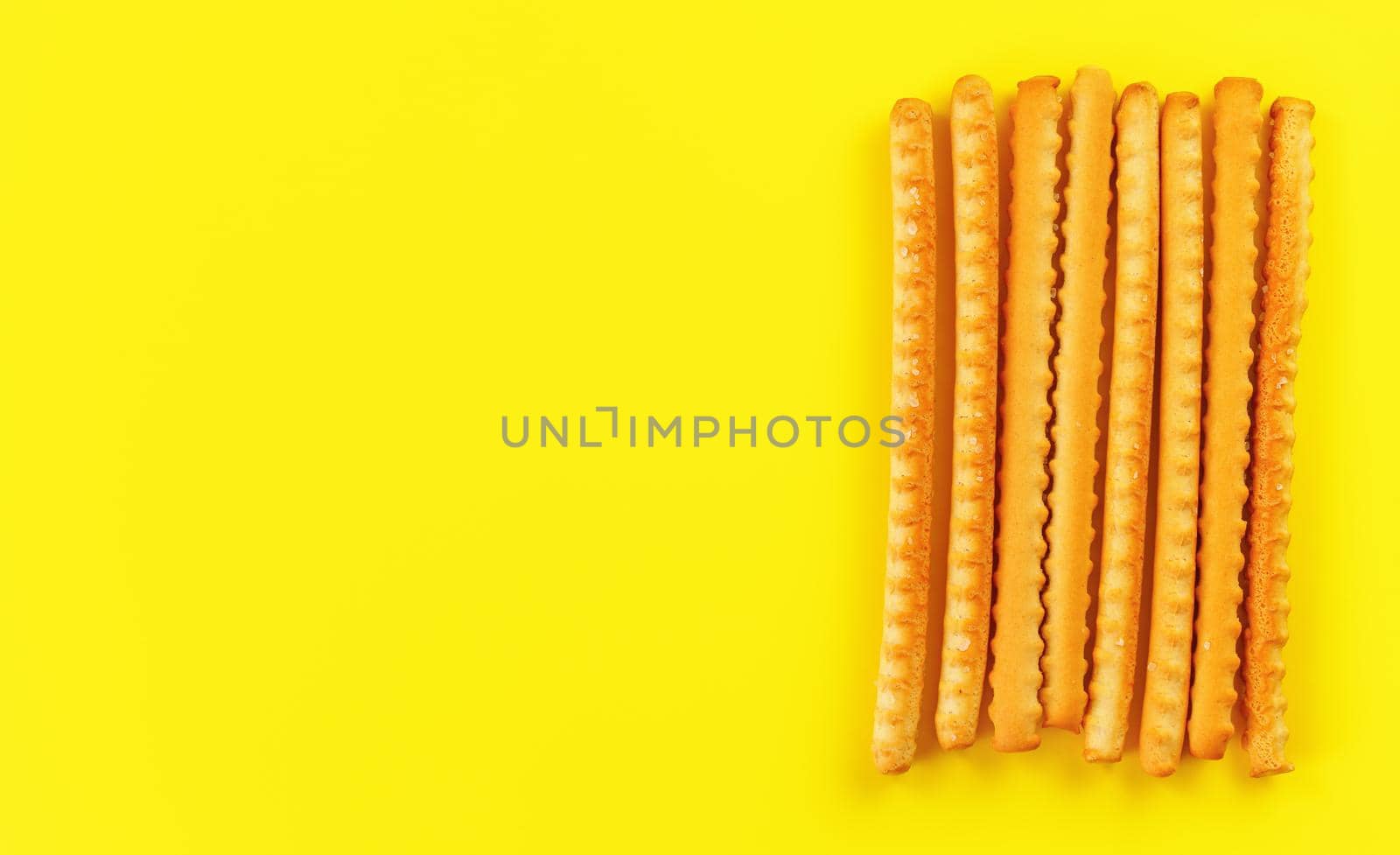 Grissini, also known as breadsticks on yellow board, view from above space for text left side.