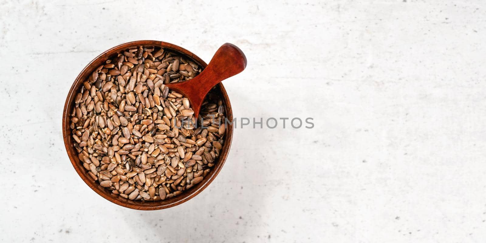 Blessed milk thistle seeds - Silybum marianum - in small wooden bowl white stone like board, view from above, space for text right side by Ivanko