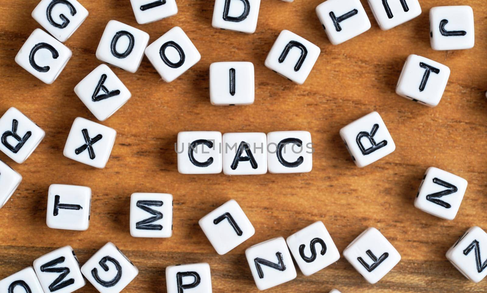 Small white and black bead cubes on wooden board, letters in middle spell CAC - Customer acquisition cost concept.