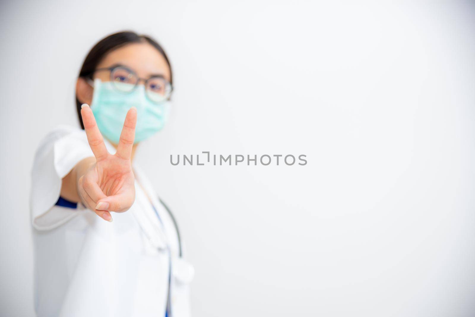 Studio portrait beautiful Asian young woman doctor raise two V shape finger wear a mask to safety Coronavirus to support in the fight against disease epidemic COVID 19 concept on blank gray background