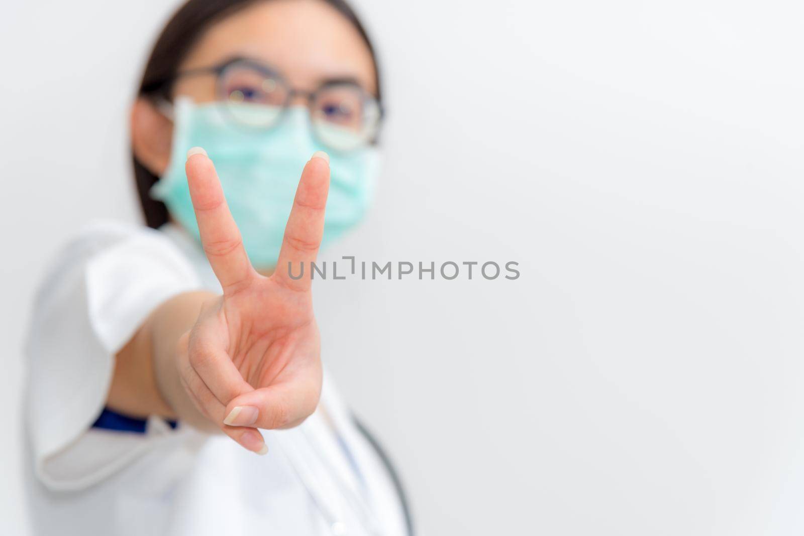 Studio portrait closeup two V shape finger of Asian young woman doctor wear a mask safety to Coronavirus for support in the fight against disease epidemic COVID 19, concept on blank gray background