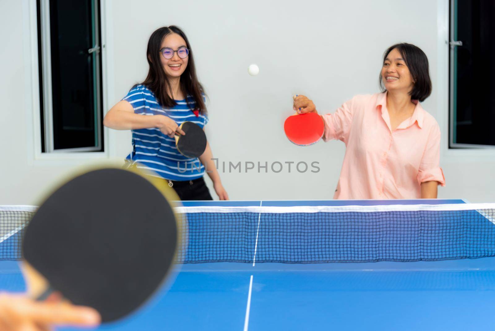 Asian family fun playing table tennis or Ping pong indoor together leisure with competing in sports games in the house. Mother and daughter enjoy recreation or exercise stay at home in Thailand