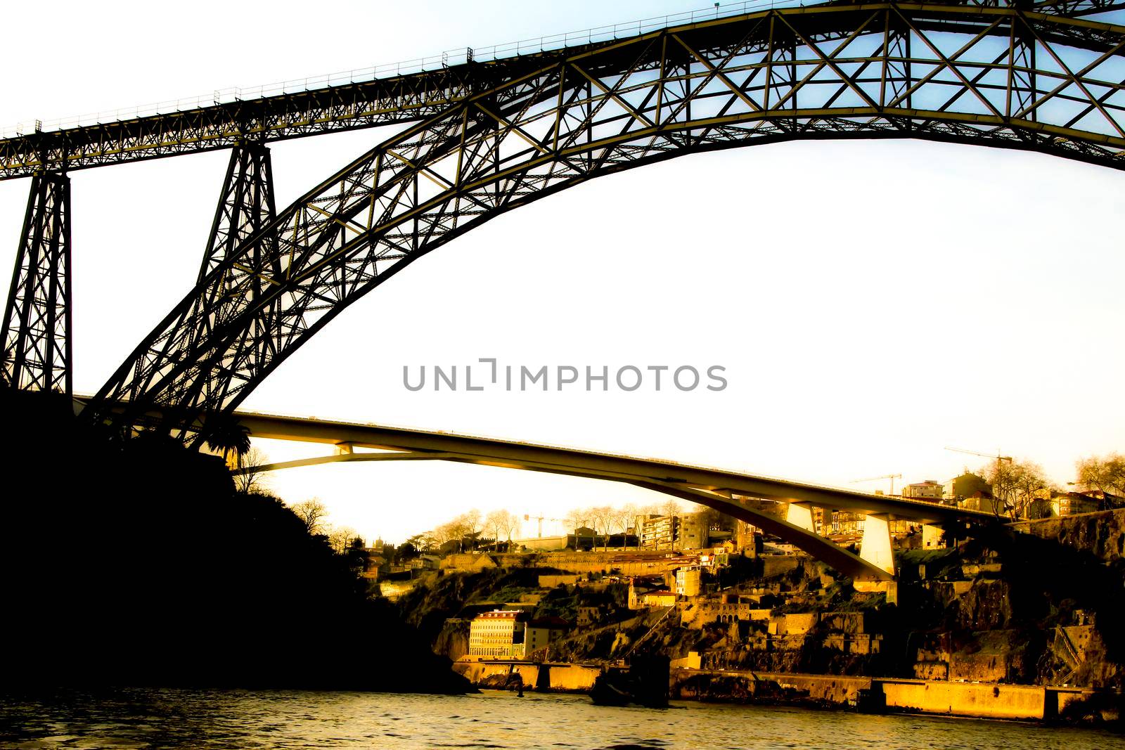 Beautiful and colossal iron bridges called Maria Pia and Ponte do Infante over the waters of the Douro River in Porto at sunset