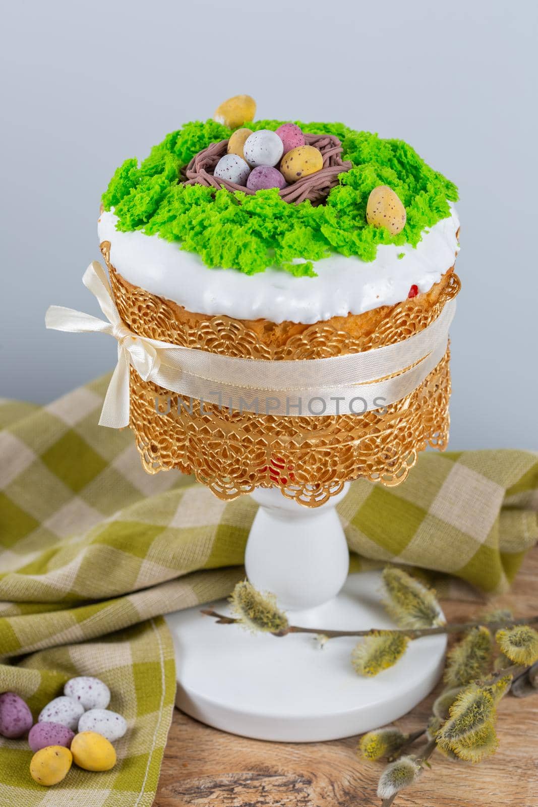 Easter cake made from yeast dough, decorated with edible moss with a nest and chocolate eggs. Easter composition on wooden table with green tablecloth