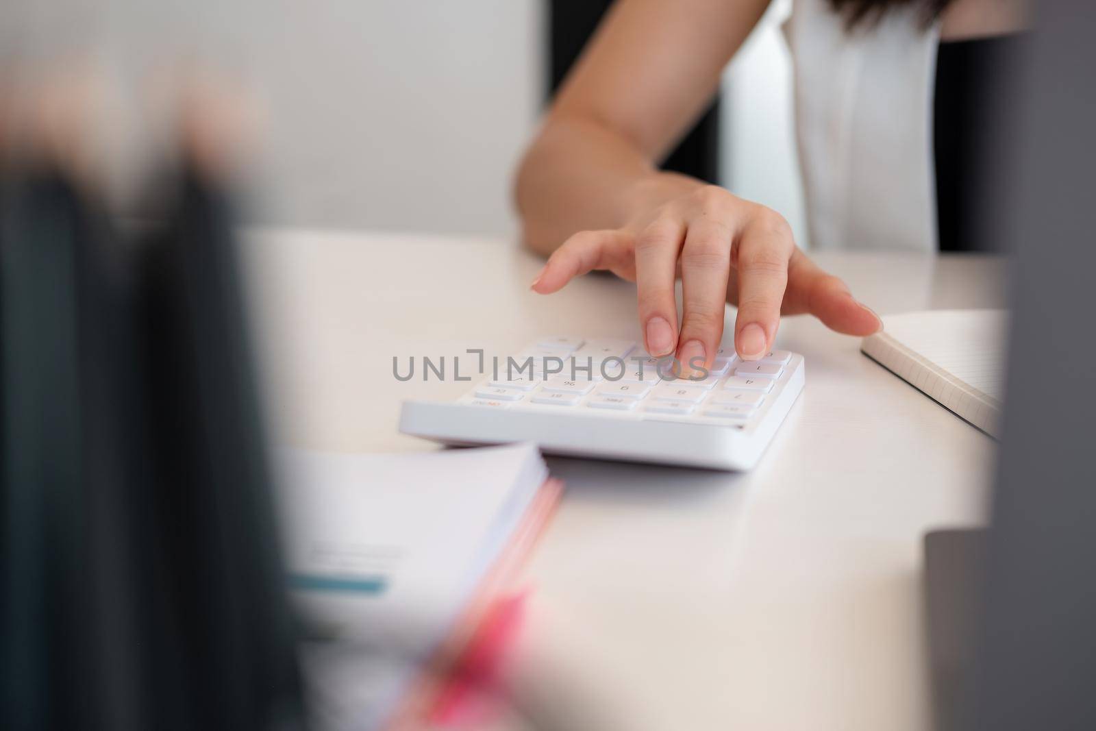 Close up woman hand using calculator and writing make note with calculate about cost at home office by nateemee