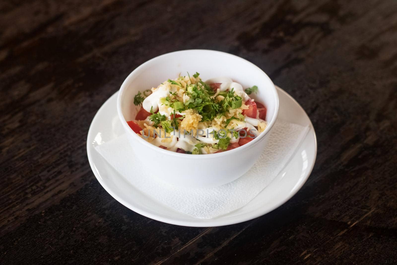 Salad with tomatoes, cheese and sauce in a plate on a wooden table