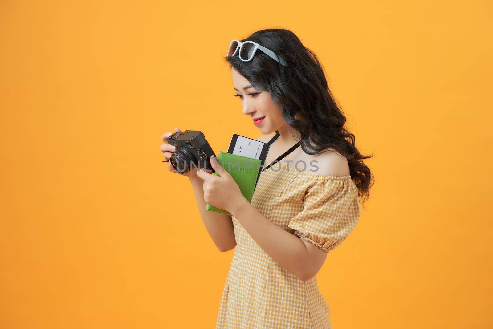 Photo of young tourist lady with camera isolated over yellow background wall holding passport with tickets