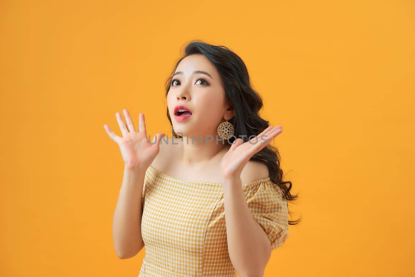 Surprised young woman shouting over yellow background. Looking at camera