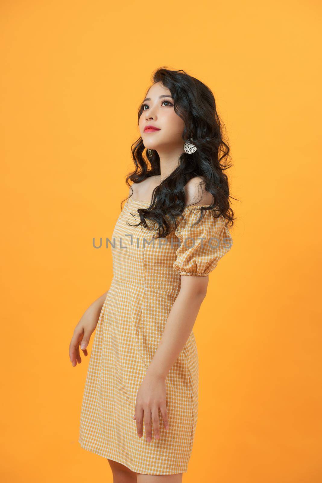 Fashionable young beautiful model posing on yellow studio background wearing dress by makidotvn