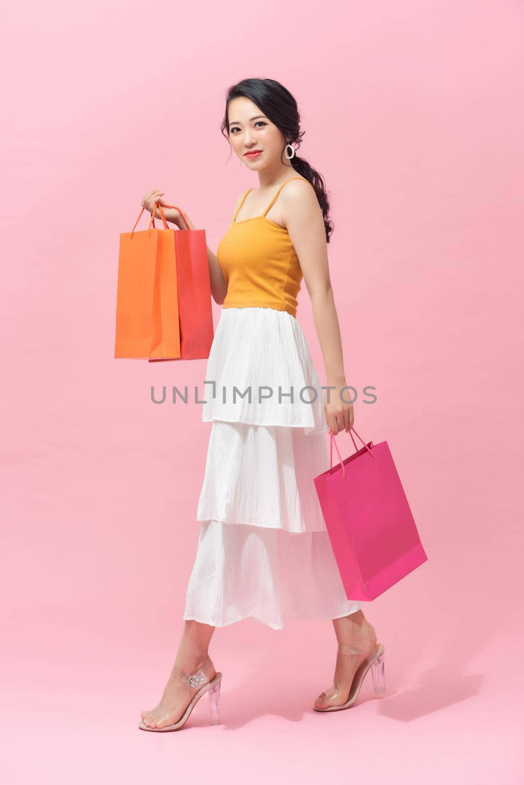 Full length portrait of a beautiful young woman posing with shopping bags, isolated against pink background by makidotvn