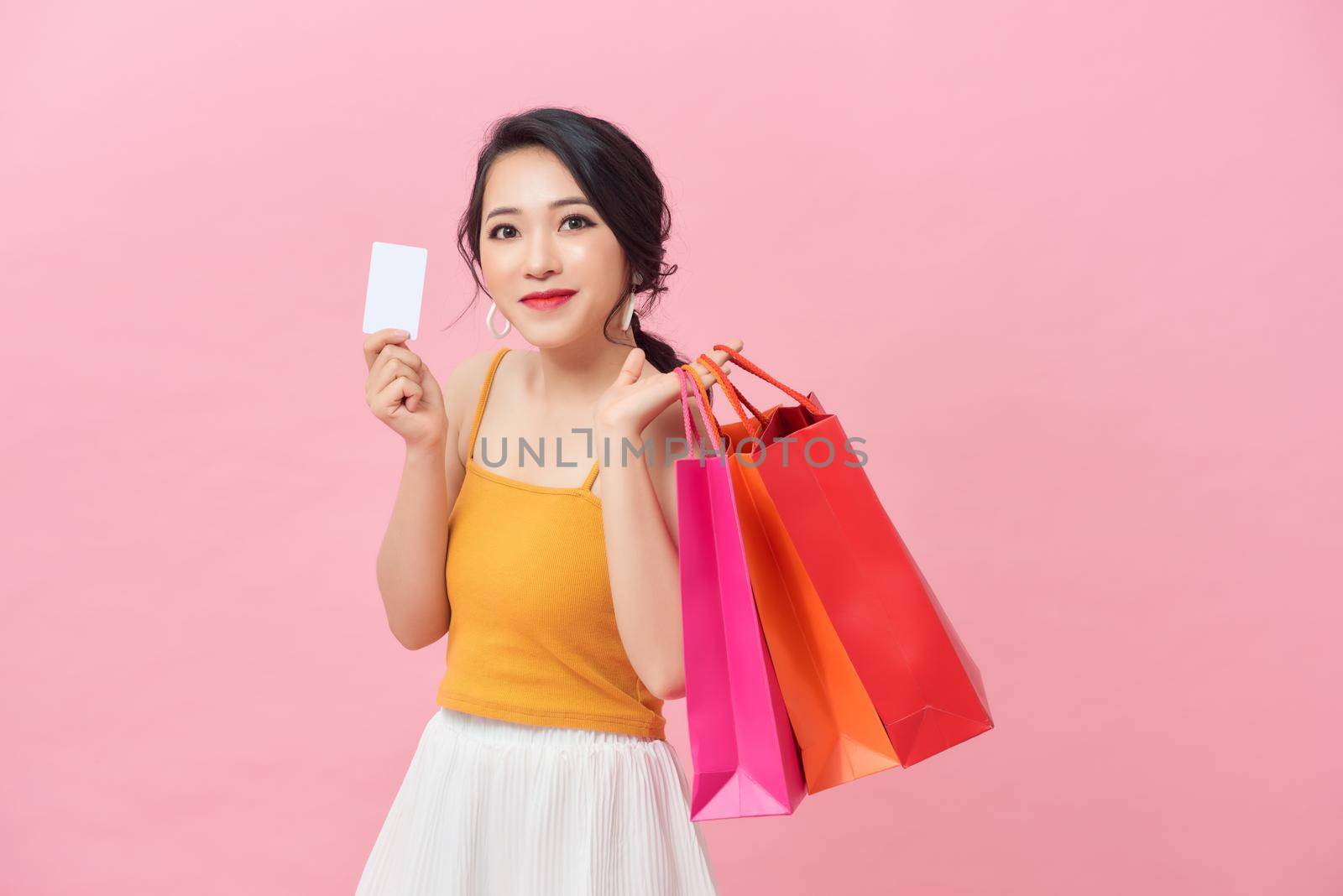 Close-up portrait of happy young Asian woman holding credit card and colorful shopping bags, isolated on pink background by makidotvn